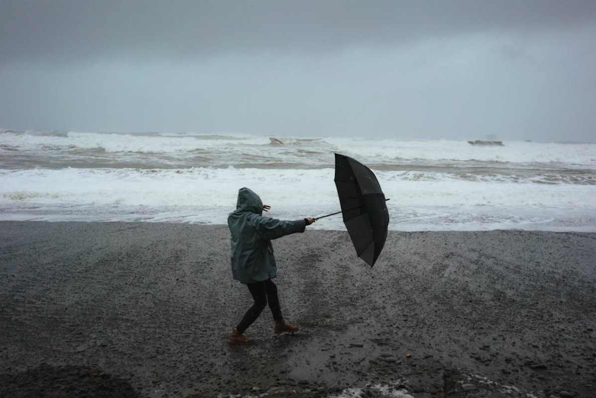 persona sulla spiaggia con il maltempo e l'ombrello in mano